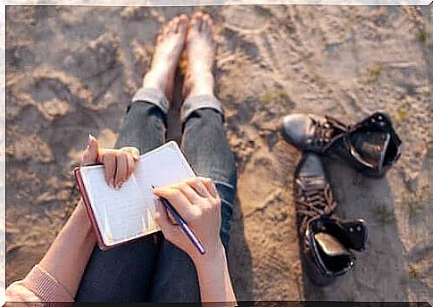 Woman sitting barefoot on a beach and writing diary