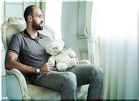 Man holding a teddy bear looking out the window