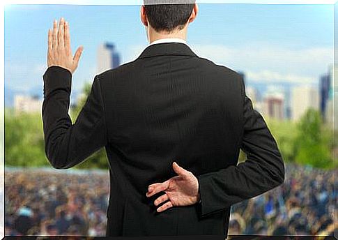 The image of a man in a suit in front of a large crowd.  He holds up one hand, as if to promise something, while the other hand crosses his fingers behind his back.  An example of post-truth.