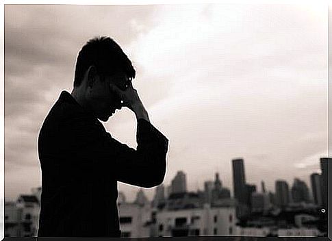 Black and white profile picture of a man holding his hand to his face.  He looks sad.