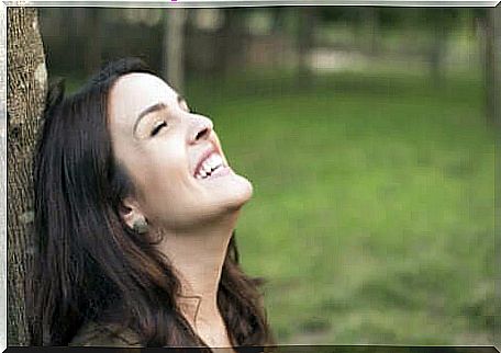 A happy woman leaning against a tree.